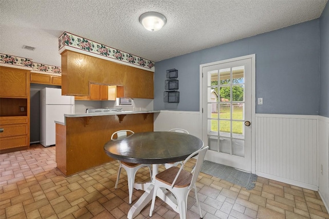 506 S Main St, Thrall, TX 76578 - kitchen featuring freestanding refrigerator, brick patterned floors, wainscoting, a peninsula, and brown cabinets