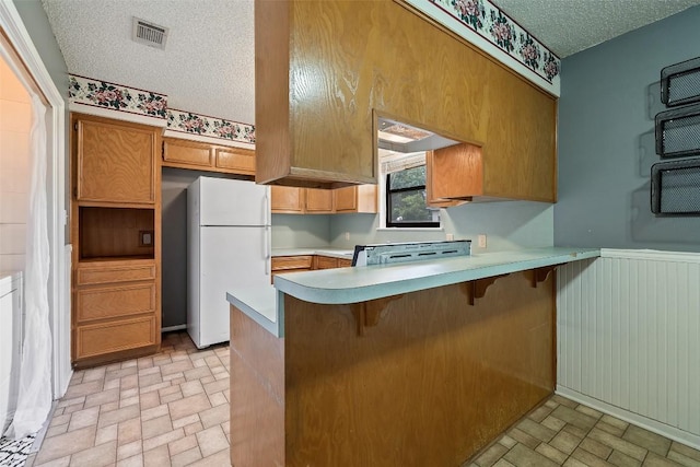 506 S Main St, Thrall, TX 76578 - kitchen featuring freestanding refrigerator, a peninsula, light countertops, a textured ceiling, and brick patterned floors