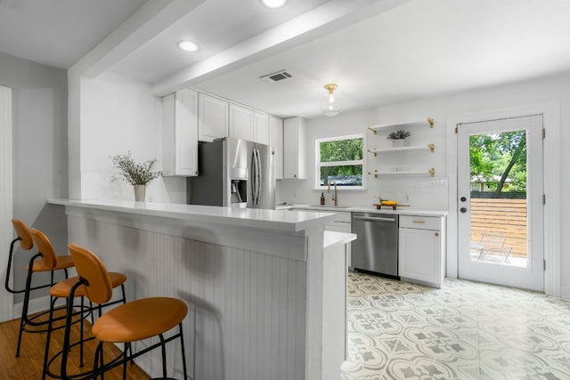 1505 Palo Duro Rd, Austin, TX 78757 - kitchen with stainless steel appliances, white cabinets, a kitchen bar, a peninsula, and light countertops