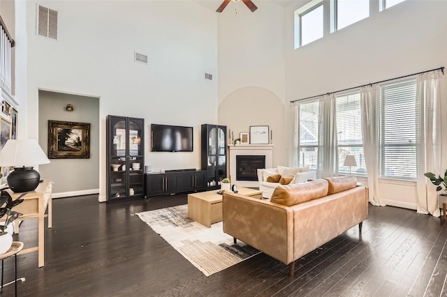 4116 Brean Down Rd, Pflugerville, TX 78660 - living room with a towering ceiling, dark wood finished floors, a glass covered fireplace, a ceiling fan, and baseboards