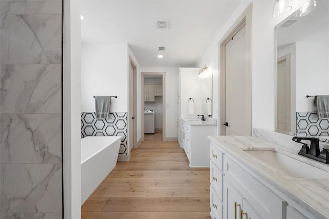 332 Claremont Dr, Belton, TX 76513 - bathroom with two vanities, a freestanding tub, wood finished floors, recessed lighting, and washer / clothes dryer