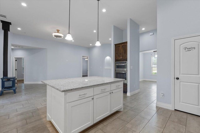 127 Medlar Dr, Cedar Creek, TX 78612 - kitchen featuring a wood stove, double oven, a kitchen island, white cabinetry, and light stone counters