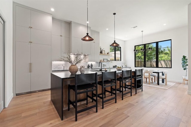 5218 Valley Oak Dr, Austin, TX 78731 - kitchen with an island with sink, light wood-type flooring, tasteful backsplash, recessed lighting, and a kitchen breakfast bar