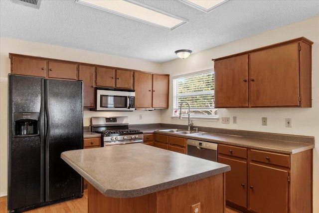 601 Wagon Wheel Trl, Pflugerville, TX 78660 - kitchen with appliances with stainless steel finishes, a sink, a textured ceiling, brown cabinets, and a center island