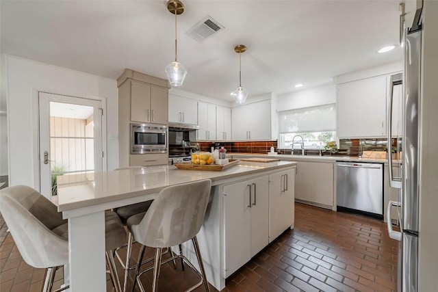 928 Porpoise St, Lakeway, TX 78734 - kitchen featuring appliances with stainless steel finishes, tasteful backsplash, light countertops, brick floors, and hanging light fixtures