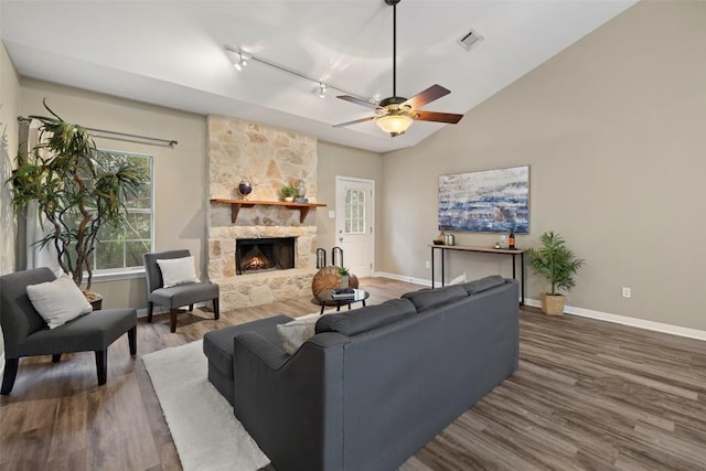 1301 S Quinlan Park Rd, Austin, TX 78732 - living room featuring rail lighting, wood finished floors, baseboards, a stone fireplace, and vaulted ceiling