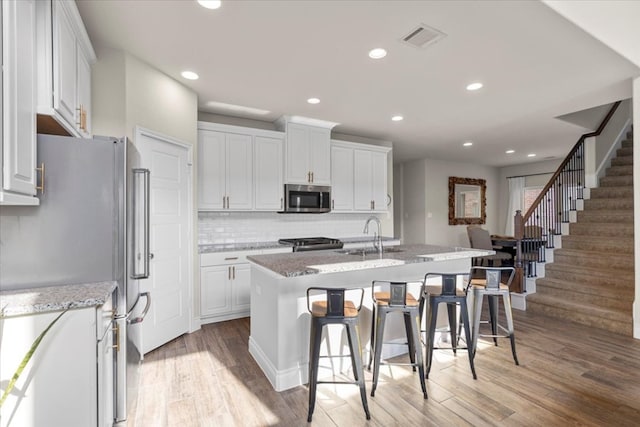 6500 Llano Stage Trl, Austin, TX 78738 - kitchen featuring stainless steel appliances, light wood-style floors, an island with sink, decorative backsplash, and white cabinets