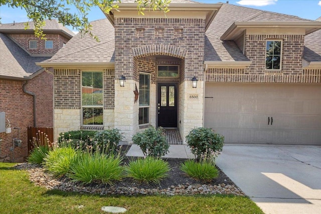 6500 Llano Stage Trl, Austin, TX 78738 - view of exterior entry with stone siding, concrete driveway, a shingled roof, a garage, and brick siding