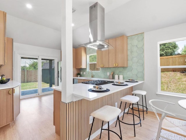 2401 Lendall Ln, Austin, TX 78744 - kitchen featuring island range hood, light wood-style flooring, a kitchen bar, and tasteful backsplash