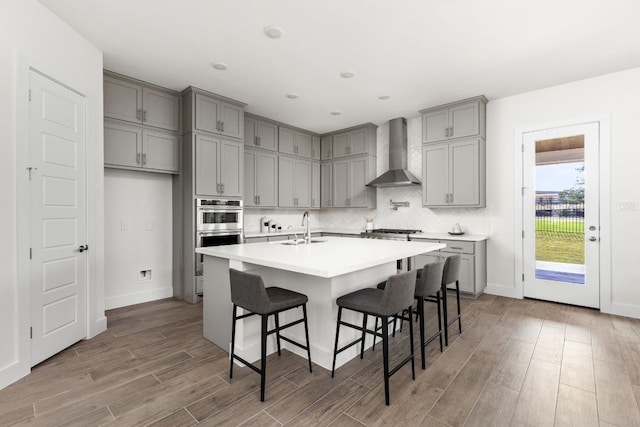 904 Arundel Rd, Lakeway, TX 78738 - kitchen with wall chimney range hood, gray cabinets, wood finished floors, appliances with stainless steel finishes, and baseboards