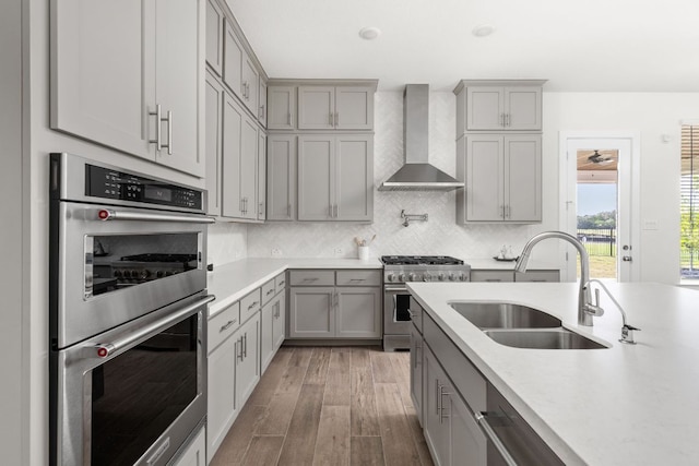 904 Arundel Rd, Lakeway, TX 78738 - kitchen featuring appliances with stainless steel finishes, wall chimney exhaust hood, gray cabinets, light countertops, and wood finished floors