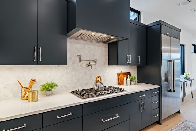 4303 Hank Ave, Austin, TX 78745 - kitchen with premium range hood, stainless steel appliances, light countertops, light wood finished floors, and decorative backsplash