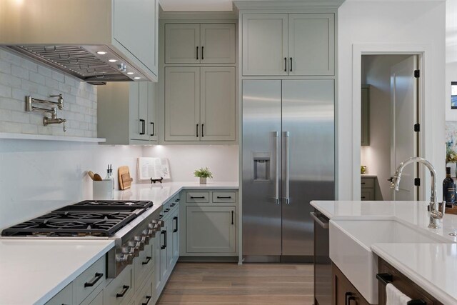 1207 Aggie Ln, Austin, TX 78757 - kitchen featuring appliances with stainless steel finishes, light countertops, decorative backsplash, light wood-style flooring, and wall chimney range hood