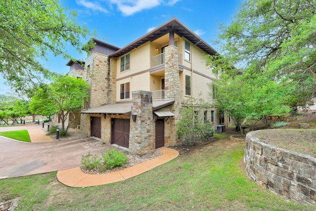 6712 Lantern View Dr Unit 303, Jonestown, TX 78645 - rear view of house featuring stone siding, a garage, driveway, stucco siding, and a lawn