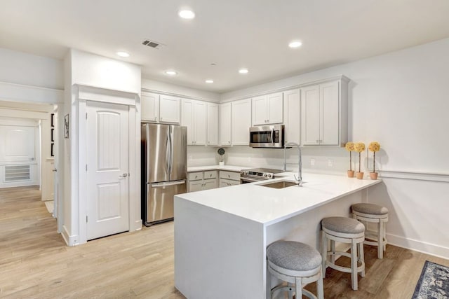 6712 Lantern View Dr Unit 303, Jonestown, TX 78645 - kitchen with appliances with stainless steel finishes, a peninsula, a kitchen breakfast bar, light wood finished floors, and light countertops