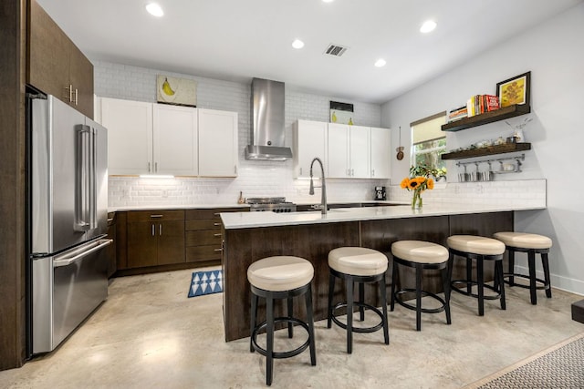 2100 E 10th St, Austin, TX 78702 - kitchen featuring high end fridge, wall chimney exhaust hood, light countertops, a breakfast bar area, and dark brown cabinetry