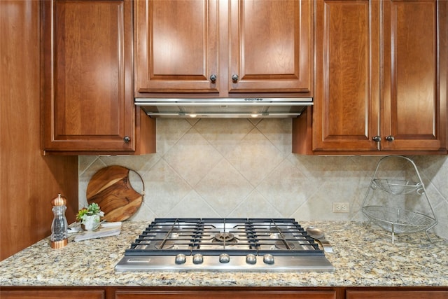 218 Duck Creek Ln, Georgetown, TX 78633 - kitchen featuring stainless steel gas cooktop, under cabinet range hood, decorative backsplash, light stone countertops, and brown cabinets