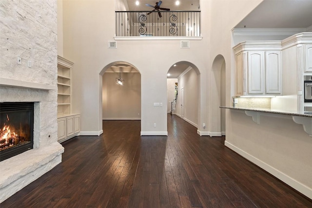 1036 Liberty Park Dr Unit 401/4A, Austin, TX 78746 - unfurnished living room featuring ceiling fan, dark wood-type flooring, baseboards, a stone fireplace, and a towering ceiling