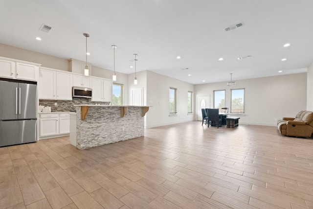 757 Canyon Bnd, Canyon Lake, TX 78133 - kitchen featuring appliances with stainless steel finishes, open floor plan, a kitchen bar, tasteful backsplash, and white cabinets