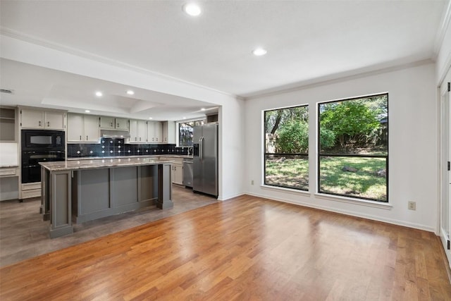 1302 Wilderness Dr, Austin, TX 78746 - kitchen featuring black appliances, recessed lighting, under cabinet range hood, a kitchen island, and tasteful backsplash