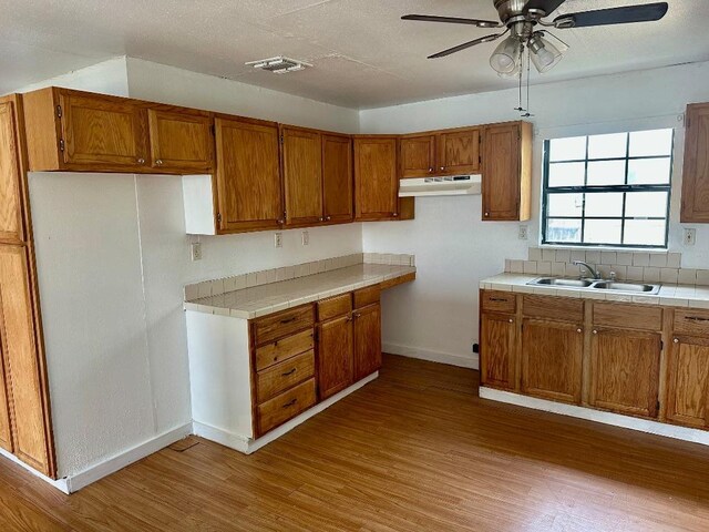 411 N Swenson St Unit 411, Falls City, TX 78113 - kitchen with under cabinet range hood, a sink, brown cabinets, and wood finished floors