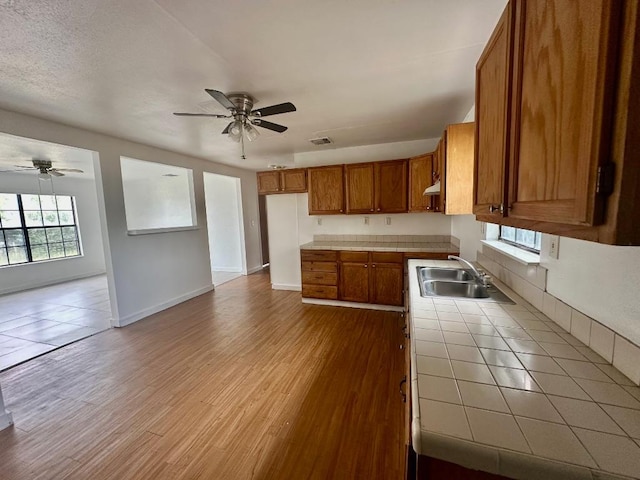 411 N Swenson St Unit 411, Falls City, TX 78113 - kitchen with tile countertops, brown cabinetry, ceiling fan, a sink, and wood finished floors