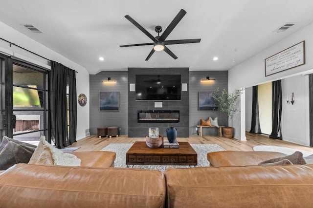 150 Wandering Oak Cir, Burnet, TX 78611 - living area featuring wood finished floors, an accent wall, ceiling fan, a large fireplace, and recessed lighting