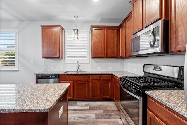 529 Cinnamon Teal Ln, Leander, TX 78641 - kitchen featuring stainless steel appliances, a sink, light wood-style floors, decorative light fixtures, and brown cabinetry