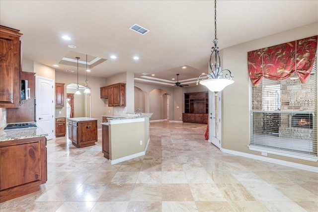 118 NE Verrena Way, Georgetown, TX 78628 - kitchen with arched walkways, open floor plan, ceiling fan, brown cabinetry, and a raised ceiling