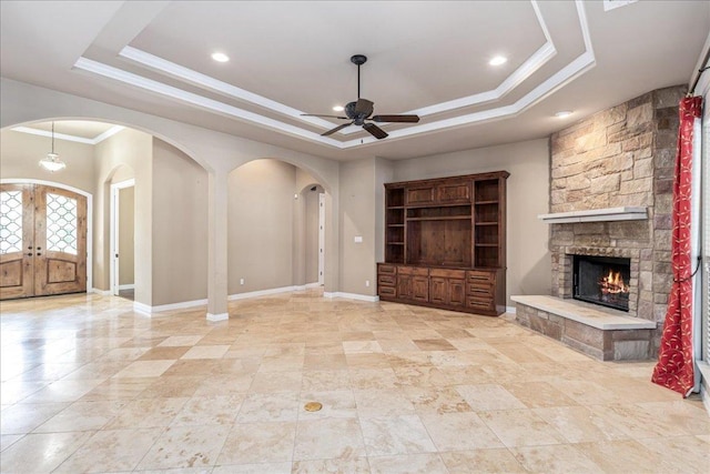 118 NE Verrena Way, Georgetown, TX 78628 - unfurnished living room with arched walkways, a raised ceiling, ceiling fan, a stone fireplace, and crown molding