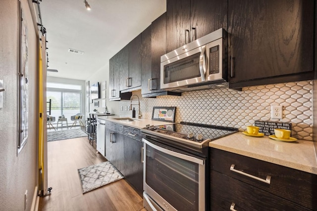 3114 S Congress Ave Unit 304, Austin, TX 78704 - kitchen featuring stainless steel appliances, a sink, light wood finished floors, dark brown cabinets, and decorative backsplash