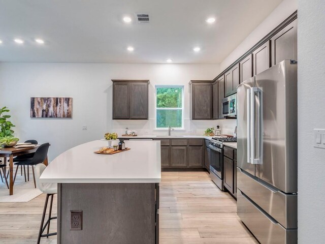 1108 Floradale Dr, Austin, TX 78753 - kitchen with stainless steel appliances, light wood-type flooring, a kitchen island, dark brown cabinets, and recessed lighting