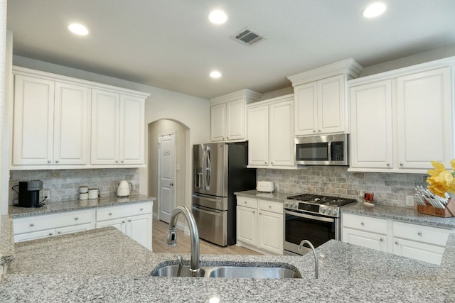 550 Cortona Ln, Georgetown, TX 78628 - kitchen featuring appliances with stainless steel finishes, a sink, arched walkways, white cabinetry, and recessed lighting