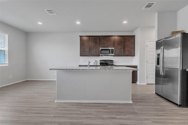 113 Bent Creek Ln, Georgetown, TX 78628 - kitchen with stainless steel appliances, dark brown cabinetry, light wood-style flooring, a center island with sink, and recessed lighting
