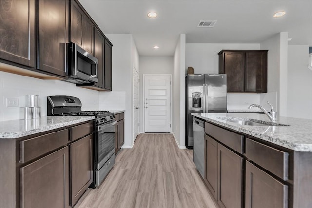 113 Bent Creek Ln, Georgetown, TX 78628 - kitchen with appliances with stainless steel finishes, light stone counters, dark brown cabinetry, light wood-type flooring, and recessed lighting