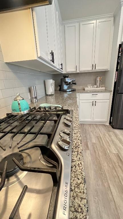 157 Monroe Dr, Kyle, TX 78640 - kitchen with stainless steel gas cooktop, white cabinets, freestanding refrigerator, and decorative backsplash