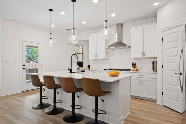 1305 Crescent Ln, Georgetown, TX 78633 - kitchen with wall chimney range hood, a sink, tasteful backsplash, a kitchen island with sink, and light wood-style flooring