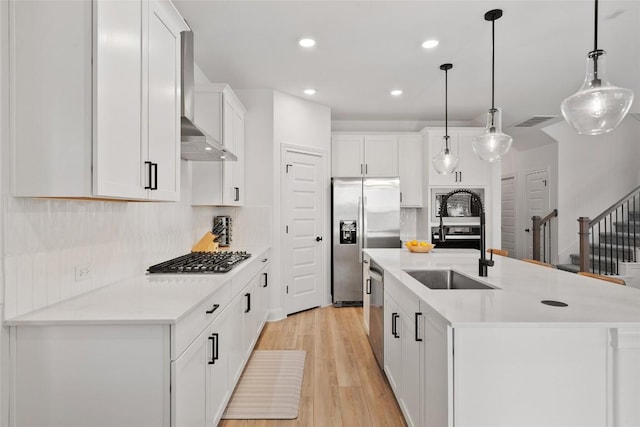 1305 Crescent Ln, Georgetown, TX 78633 - kitchen with stainless steel appliances, wall chimney range hood, a sink, light wood-style floors, and white cabinets