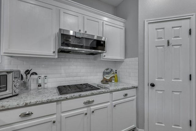 745 Bent Wood Pl, Round Rock, TX 78665 - kitchen featuring stainless steel microwave, stovetop, tasteful backsplash, white cabinetry, and light stone countertops