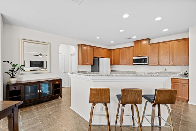 122 Mancos Dr, Georgetown, TX 78626 - kitchen featuring stainless steel microwave, freestanding refrigerator, a kitchen breakfast bar, light tile patterned floors, and recessed lighting