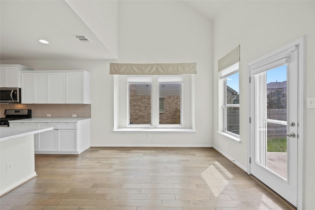 6724 Leonardo Dr, Round Rock, TX 78665 - kitchen featuring appliances with stainless steel finishes, light countertops, white cabinetry, light wood-style flooring, and high vaulted ceiling