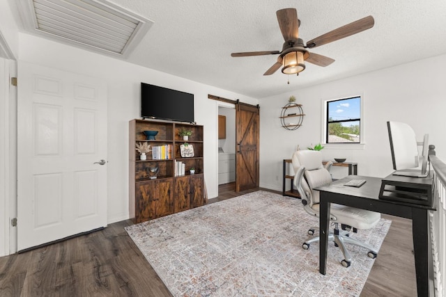 744 Jim Bowie Dr, Spicewood, TX 78669 - home office with a barn door, ceiling fan, dark wood-style flooring, and a textured ceiling