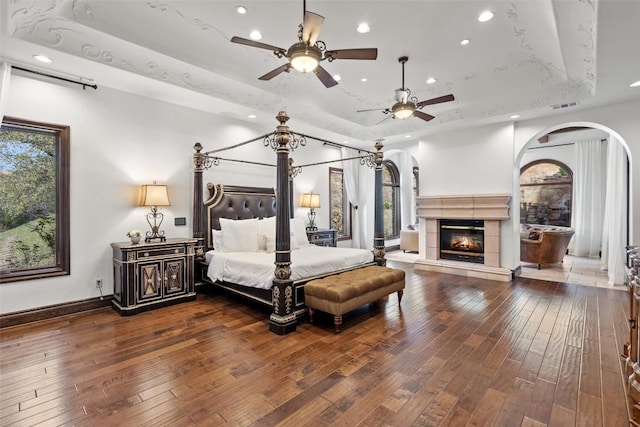 604 Logans Ln, Austin, TX 78746 - bedroom featuring a tray ceiling, arched walkways, recessed lighting, hardwood / wood-style flooring, and a tile fireplace