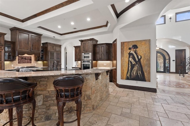 604 Logans Ln, Austin, TX 78746 - kitchen featuring arched walkways, stainless steel oven, a breakfast bar area, light stone countertops, and ornamental molding