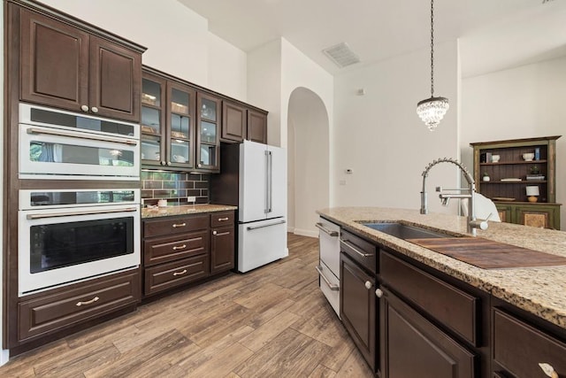 310 Lauren Trl, Cedar Park, TX 78613 - kitchen with white appliances, arched walkways, dark brown cabinets, decorative light fixtures, and backsplash