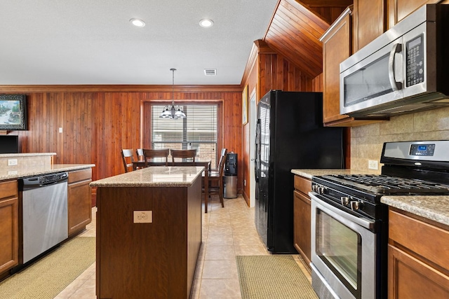 113 Blossom Valley Strm, Buda, TX 78610 - kitchen featuring stainless steel appliances, a center island, decorative backsplash, wood walls, and light tile patterned flooring