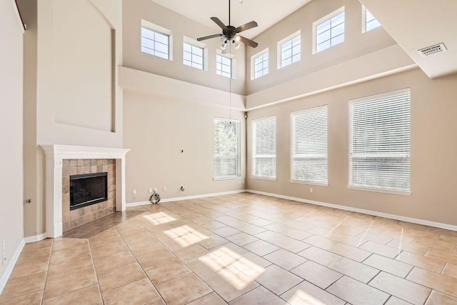 7701 Crackling Creek Dr, Austin, TX 78736 - unfurnished living room with ceiling fan, light tile patterned flooring, a tiled fireplace, a high ceiling, and baseboards