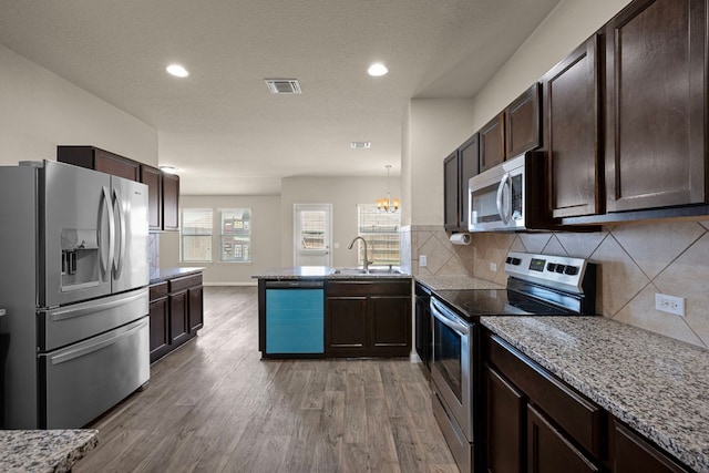 144 Sulphur River Loop, Hutto, TX 78634 - kitchen with appliances with stainless steel finishes, a sink, a peninsula, dark brown cabinetry, and wood finished floors