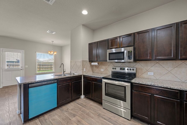 144 Sulphur River Loop, Hutto, TX 78634 - kitchen featuring stainless steel appliances, a sink, a chandelier, a peninsula, and light wood-style floors