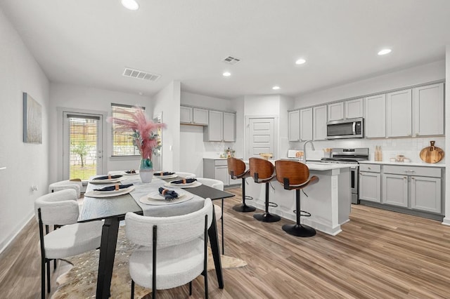 7809 Linnie Ln, Austin, TX 78724 - kitchen with appliances with stainless steel finishes, gray cabinetry, light wood-style flooring, an island with sink, and recessed lighting